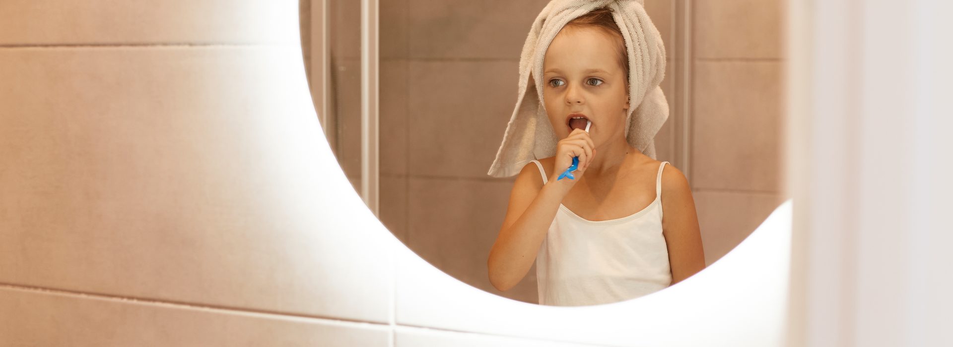 Ujęcie w pomieszczeniu słodkiej dziewczyny, która myje zęby w łazience, stoi przed lustrem, owija głowę ręcznikiem, zabiegi higieniczne rano lub przed pójściem spać